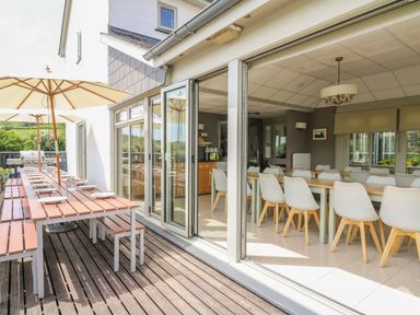 An outdoor dining area with long wooden tables and umbrellas next to an indoor dining room with white chairs and tables at Llety Ceiro in Bow Street Wales