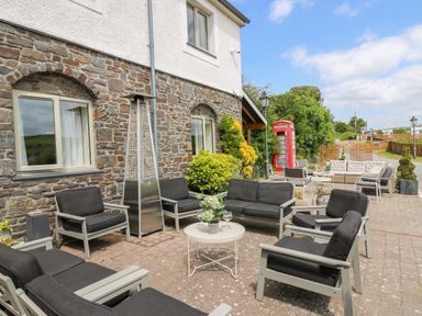 An outdoor patio with seating arranged around tables beside a stone building with windows and plants a red telephone box is visible at Llety Ceiro Bow Street Wales