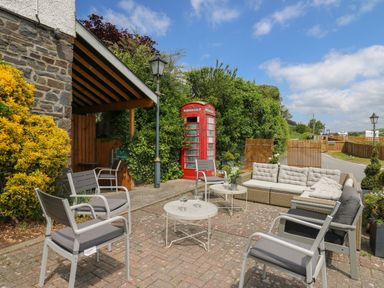 An outdoor seating area with chairs tables and a sofa near a red telephone booth at Llety Ceiro in Bow Street Wales
