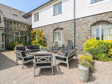 Outdoor seating area with black cushioned chairs and sofas around a table in front of a stone building with the sign Llety Ceiro in Bow Street Wales