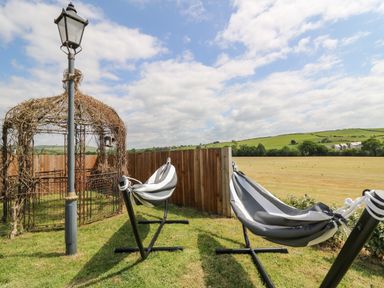 Two striped hammocks on stands near a wooden fence and a metal gazebo with a lamp post in a grassy yard at Llety Ceiro in Bow Street Wales