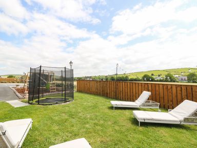 A fenced backyard with sun loungers trampoline and children's playset at Llety Ceiro Bow Street Wales