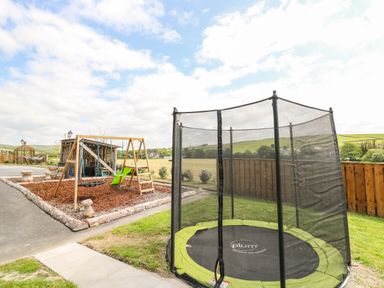 An outdoor play area with a trampoline and a wooden swing set at Llety Ceiro in Bow Street Wales