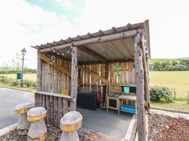 A wooden outdoor shelter with mushroom shaped stools and a play kitchen at Llety Ceiro in Bow Street Wales