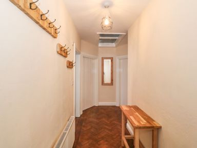 A hallway with wooden coat hooks on the wall a wooden table a ceiling light a wall mirror and parquet flooring at Ty Garth in Benllech