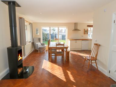 A dining area with a wooden table and chairs next to a kitchen with white cabinets and a stove at Ty Garth in Benllech