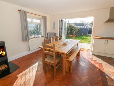 A dining area with wooden table and chairs next to an open door showing a garden at Ty Garth in Benllech