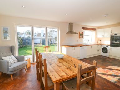 A kitchen with wooden dining table chairs and armchair next to sliding glass doors leading to garden at Ty Garth in Benllech