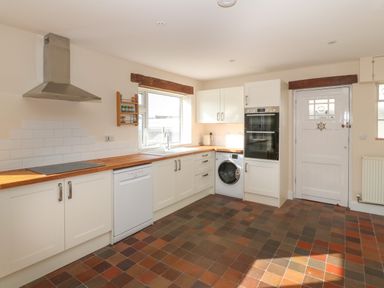 A kitchen with white cabinets wooden countertops a dishwasher washing machine built in oven and white door at Ty Garth in Benllech