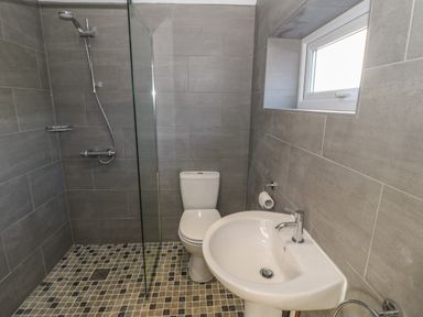 A bathroom with a shower, toilet, sink, and window at Ty Garth in Benllech