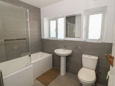 A bathroom with a bathtub shower sink toilet mirror and two windows at Ty Garth in Benllech