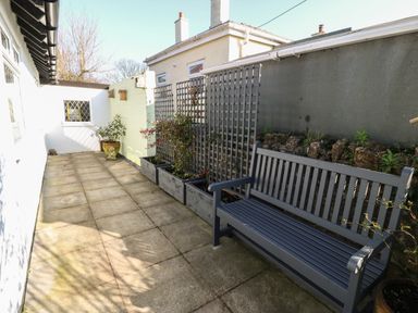 An outdoor patio area with a wooden bench potted plants and trellis at Ty Garth in Benllech