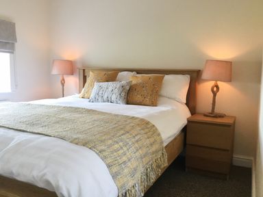 A bedroom with a wooden bed and patterned cushions next to a wooden bedside table with a lamp at Ty Garth in Benllech