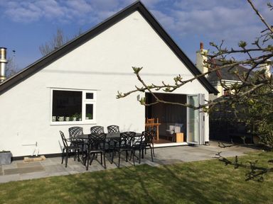 A white house with a patio table and chairs on a stone terrace and a grassy yard at Ty Garth in Benllech