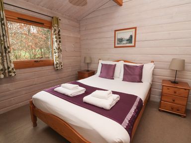 A bedroom with a wooden bed frame bedside tables lamps and a window at Barn Owl Lodge Rhayader