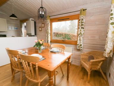 A dining area with a wooden table set for four and a wicker chair near a window at Barn Owl Lodge in Rhayader