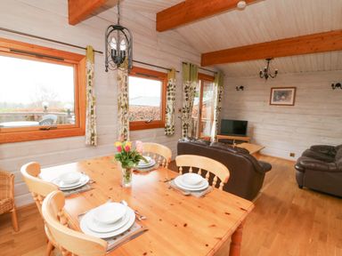 A dining area with a wooden table set for four and a living room with leather sofas and a TV at Barn Owl Lodge in Rhayader