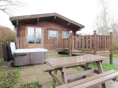 A wooden lodge with a hot tub and picnic table outside at Barn Owl Lodge in Rhayader