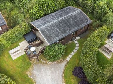 An aerial view of a small wooden cabin with a deck and outdoor furniture surrounded by greenery and paths at Barn Owl Lodge in Rhayader