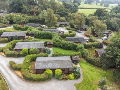An aerial view of multiple wooden lodges with surrounding greenery and gravel paths at Barn Owl Lodge in Rhayader