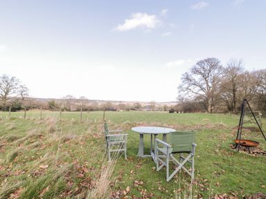 A grassy outdoor area with two chairs and a round table near a fire pit at Deer Lodge in Wimborne Minster
