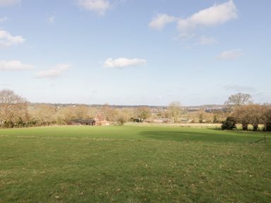A large green field with trees and houses in the distance under a blue sky at Deer Lodge in Wimborne Minster
