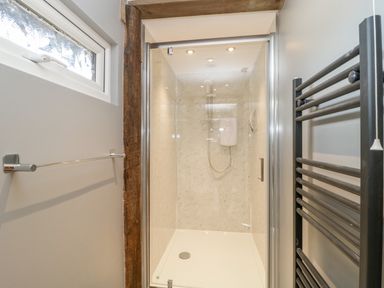 A shower enclosure with glass door a wooden beam a towel rail and a radiator in a bathroom at Deer Lodge in Wimborne Minster