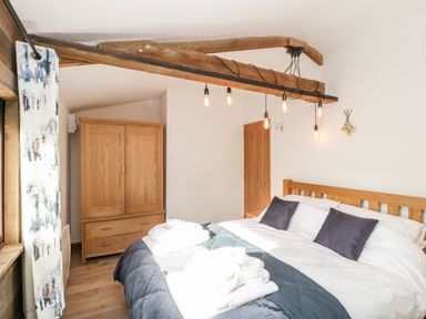 A bedroom with a bed with pillows and folded towels a wooden wardrobe and a door at Deer Lodge in Wimborne Minster