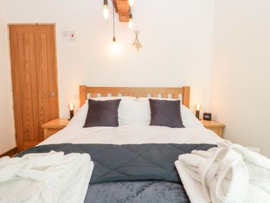 A bedroom with a wooden bedframe two pillows bedside tables lamps and robes at Deer Lodge in Wimborne Minster