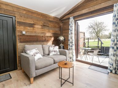A living room with a gray sofa wooden side table and opens onto a patio at Deer Lodge in Wimborne Minster