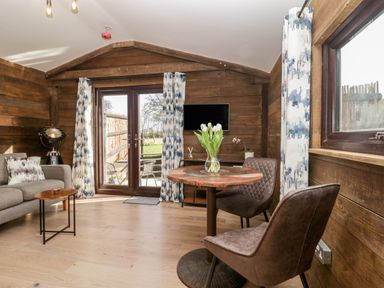A wooden room with a round table and two chairs a sofa and a TV on the wall at Deer Lodge in Wimborne Minster