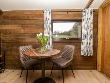 A dining area with a round wooden table and two brown chairs next to a window with curtains at Deer Lodge in Wimborne Minster