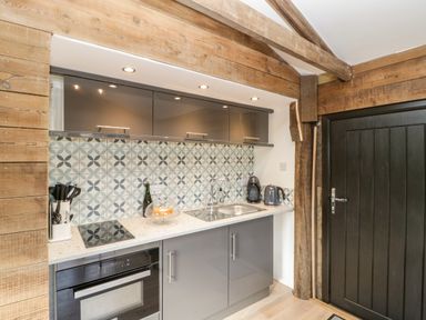 A kitchen area with a stove oven sink kettle and coffee machine and patterned tile backsplash at Deer Lodge in Wimborne Minster