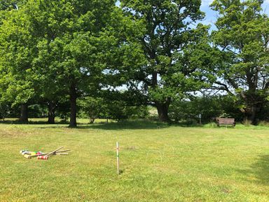 A grassy field with croquet mallets and hoops set up near large trees with a bench in the background at Deer Lodge in Wimborne Minster