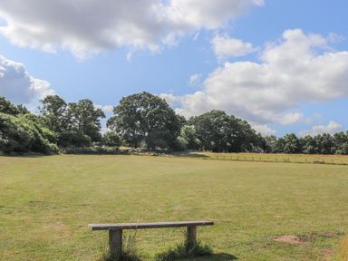 A grassy field with a wooden bench and trees under a partly cloudy sky at Deer Lodge in Wimborne Minster