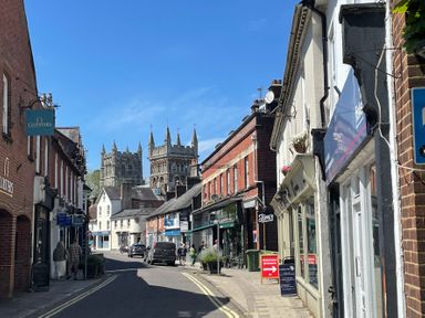 A street with shops and people walking with a large cathedral in the background at Deer Lodge in Wimborne Minster