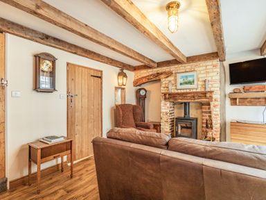A living room with wooden beams, a leather sofa, an armchair, a fireplace, a wall clock, a small table, and a mounted TV at 48 High Street in Bridlington