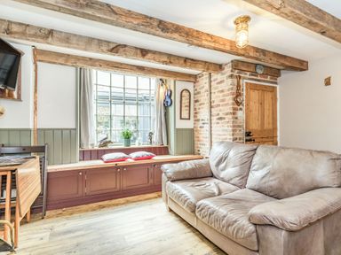 A living room with a leather sofa wooden beams window seat and a wooden door at 48 High Street in Bridlington