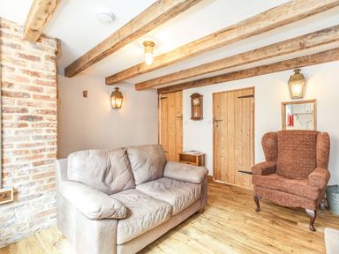 A living room with a leather sofa and armchair wooden ceiling beams and wooden doors at 48 High Street in Bridlington