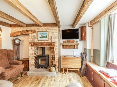 A living room with exposed wooden beams a fireplace with wood burner a wall-mounted television and a window seat at 48 High Street in Bridlington