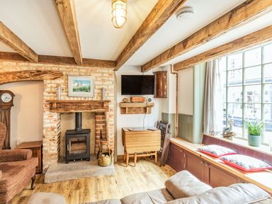 A sitting room with a brick fireplace wooden beams a wall-mounted television and a window seat at 48 High Street in Bridlington