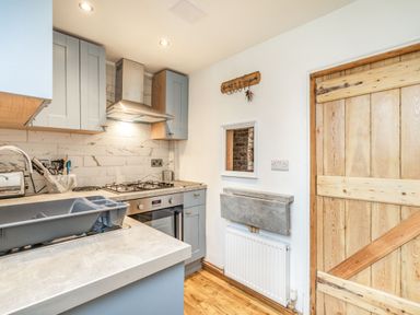 A kitchen with grey cabinets a gas stove a wooden door and a countertop with a dish rack at 48 High Street in Bridlington