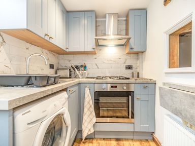 A kitchen with blue cabinets a washing machine an oven a sink and a cooker hood at 48 High Street in Bridlington