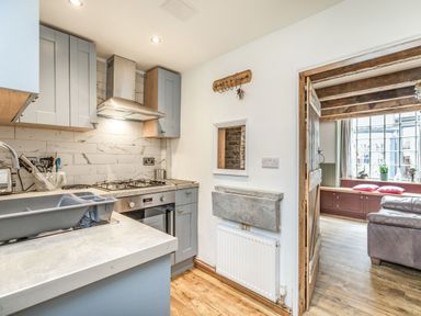 A kitchen with cupboards a gas stove and a dish drying rack next to a doorway leading to a living room at 48 High Street in Bridlington