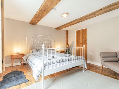 A bedroom with a white metal bed frame two wooden bedside tables with lamps a gray rug wooden floor exposed wooden ceiling beams and a gray armchair at 48 High Street Bridlington