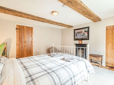 A bedroom with a bed with plaid bedding two wooden doors a small wooden bench a fireplace with a framed picture above and wooden ceiling beams at 48 High Street in Bridlington