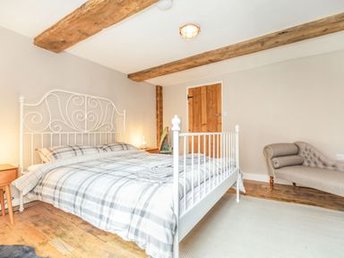 A bedroom with a white metal bed frame and plaid bedding a wooden door a beige chaise lounge and exposed wooden ceiling beams at 48 High Street Bridlington