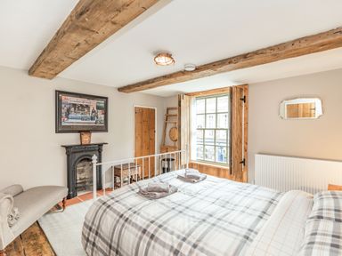 A bedroom with a bed a fireplace wooden beams and a window with wooden shutters at 48 High Street in Bridlington