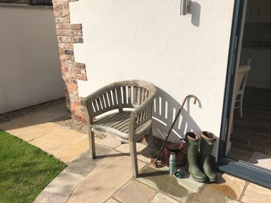 An outdoor area with a wooden chair boots an umbrella a thermos and a bag near a white wall and glass door at 1 Church Barns in Pocklington