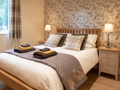 A bedroom with a wooden bed frame bedside tables with lamps folded towels on the bed and a window with curtains at Larchwood Lodge Ellon